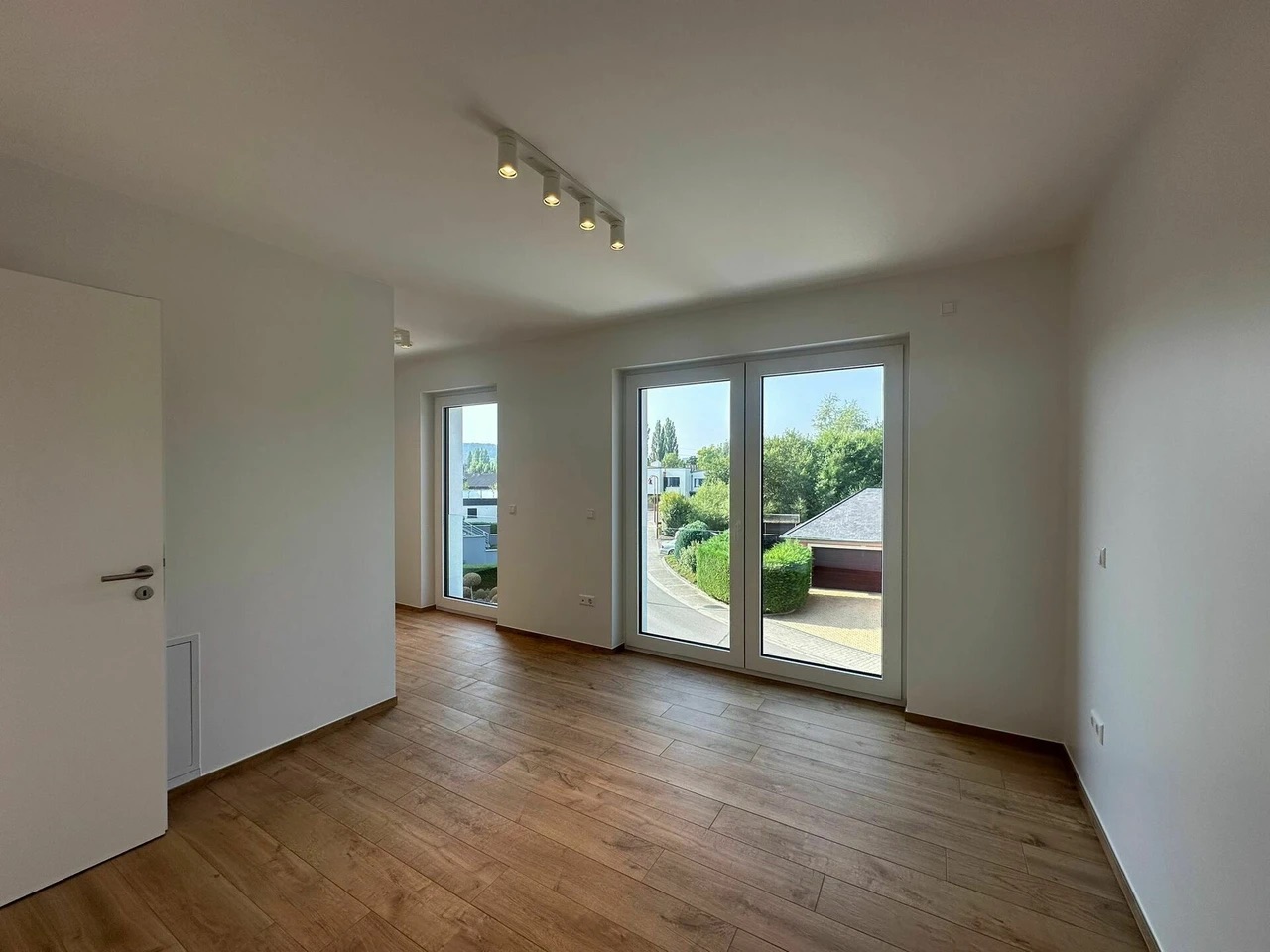 Chambre vide avec sol en parquet et grandes fenêtres donnant sur la rue